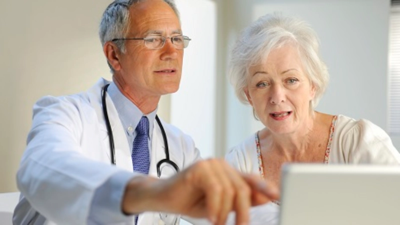 Ein Arzt und eine ältere Patientin vor dem Laptop.