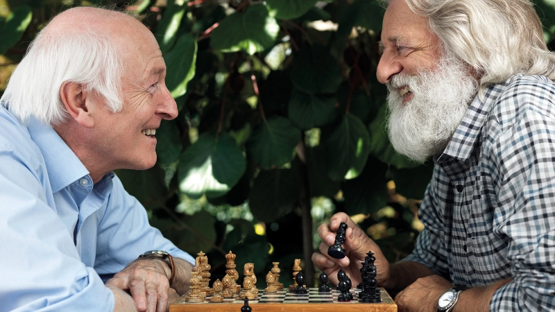 Zwei ältere Männer spielen Schach und lachen dabei