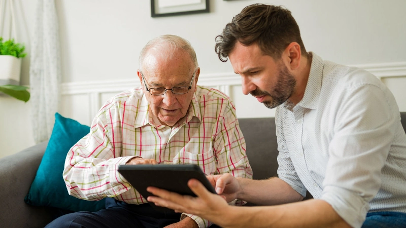 Freiwilliger von Pro Senectute erklärt Senior etwas auf dem Tablet