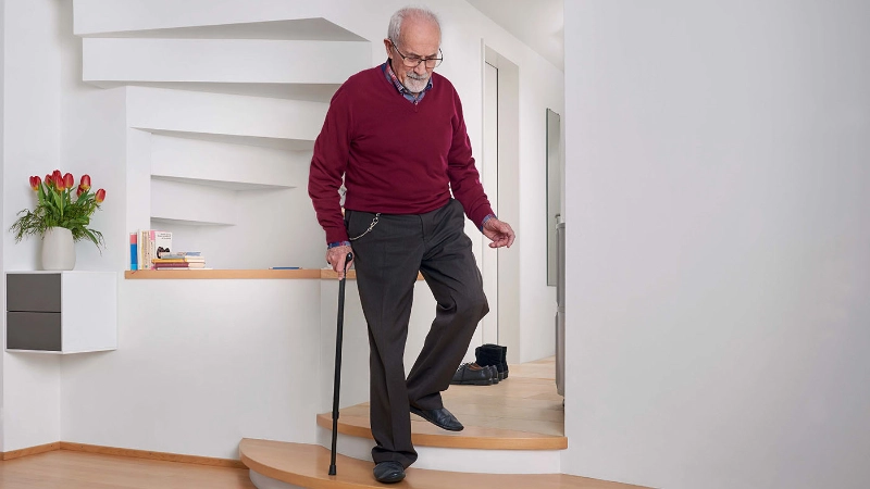 Ein älterer Mann geht vorsichtig am Stock die Treppe herunter.
