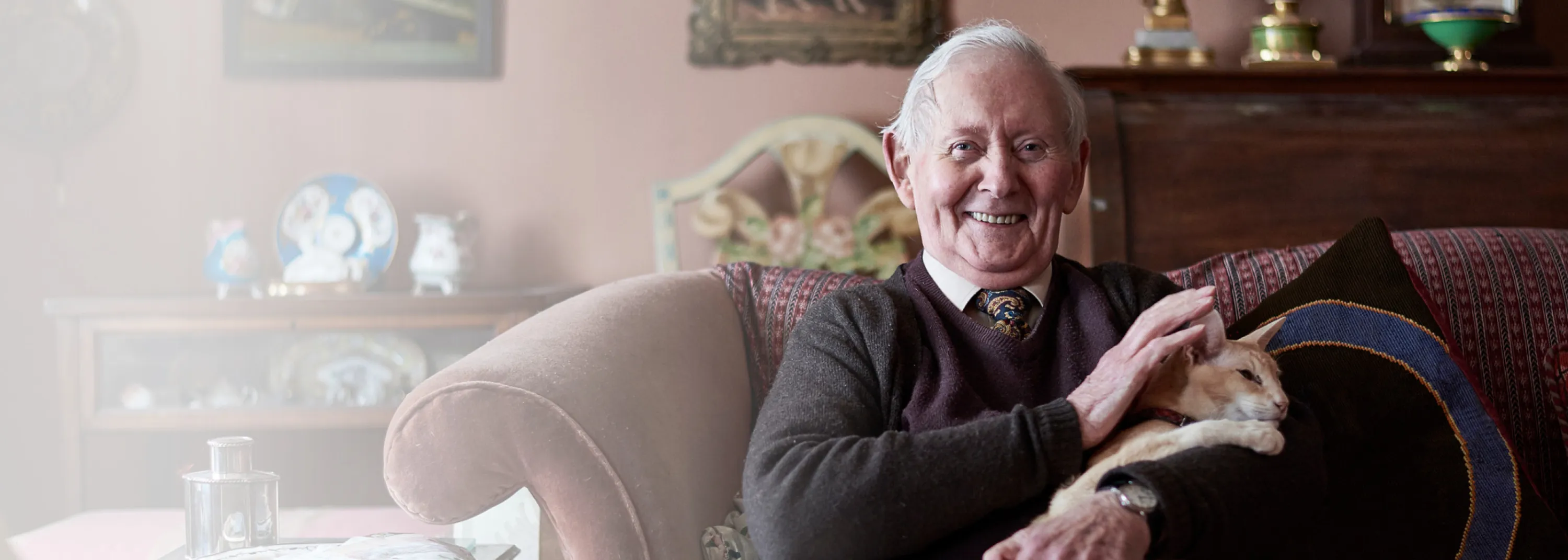Ein älterer Herr sitzt auf dem Sofa, mit einer Katze im Arm.