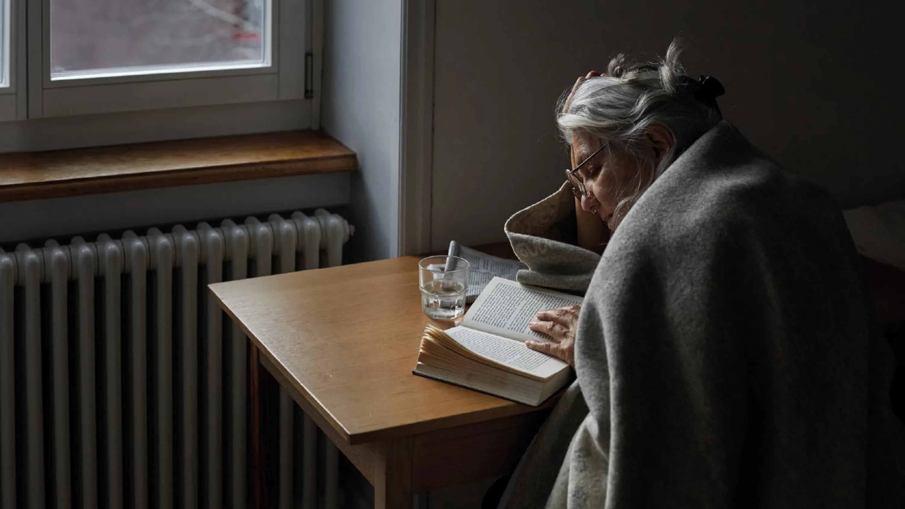 Une personne âgée avec une couverture et du thé lit un livre.