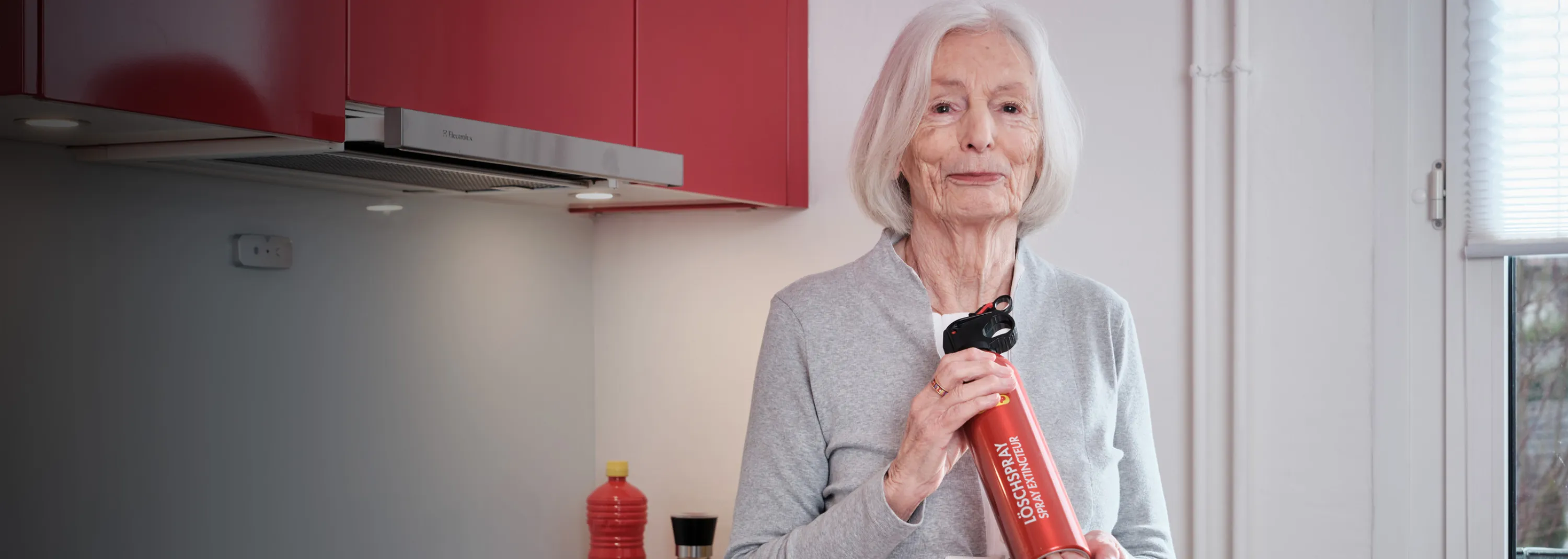 Ältere Dame hält Feuerlöscher und schaut in die Kamera